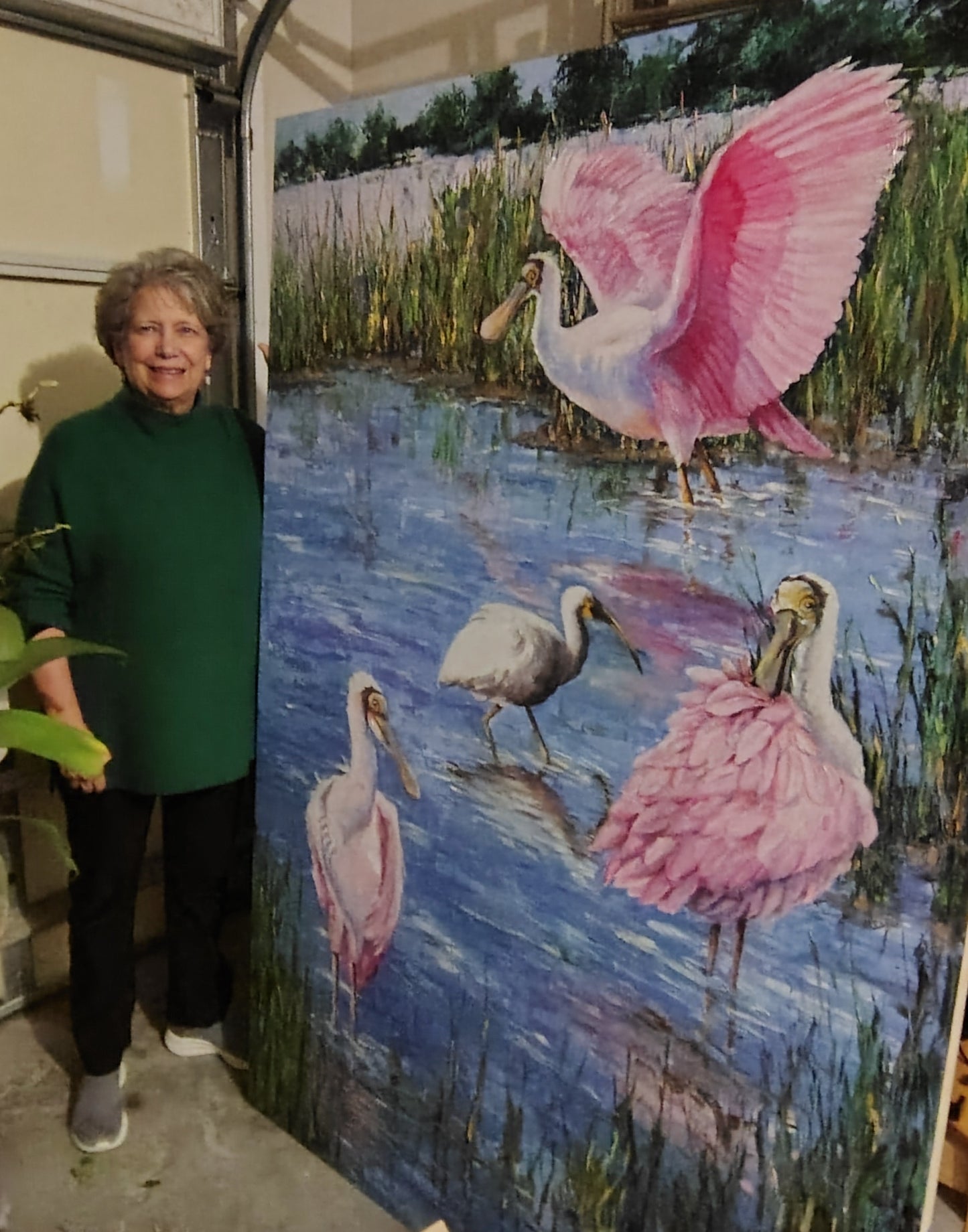 Woman standing next to a painting of pink birds in a natural setting
