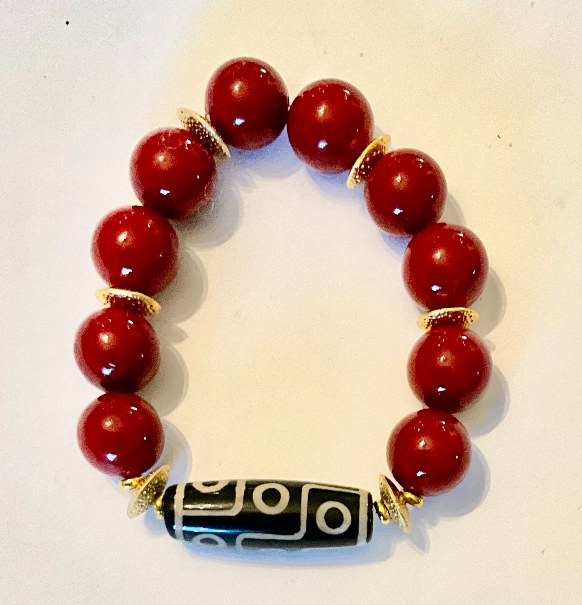 Bracelet with red beads and a black and gold central bead on a light background