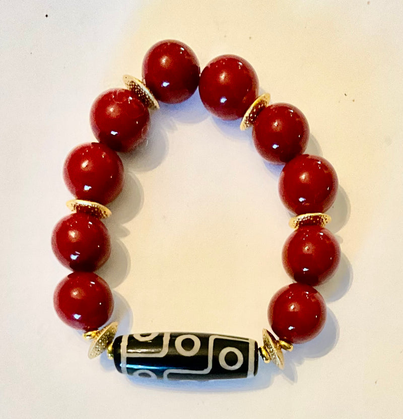 Bracelet with red beads and a black and gold central bead on a light background
