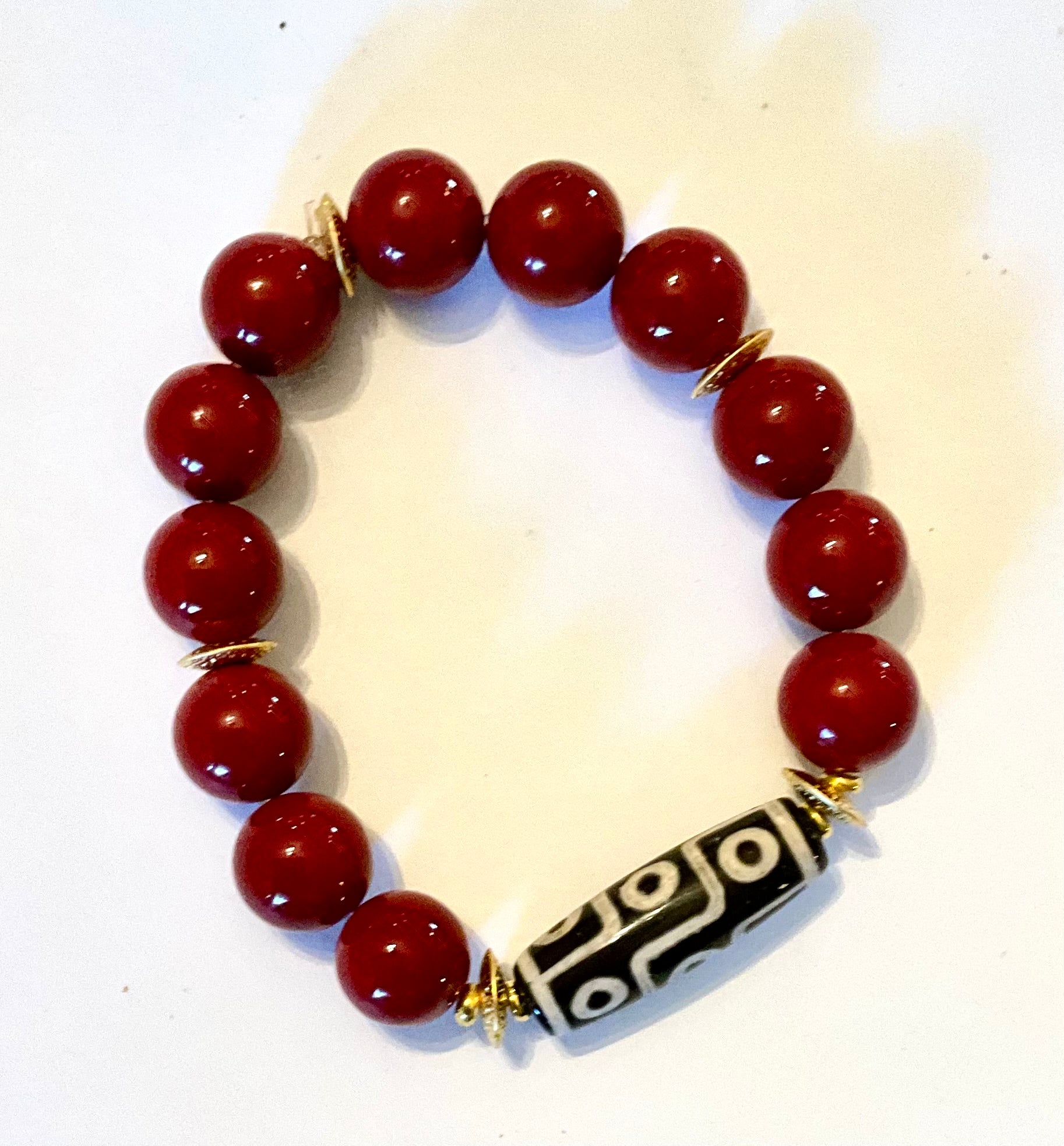 Bracelet with red beads and a black and white patterned clasp on a white background