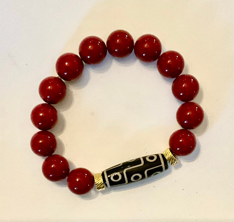 Bracelet with red beads and a black and gold patterned bead on a white background
