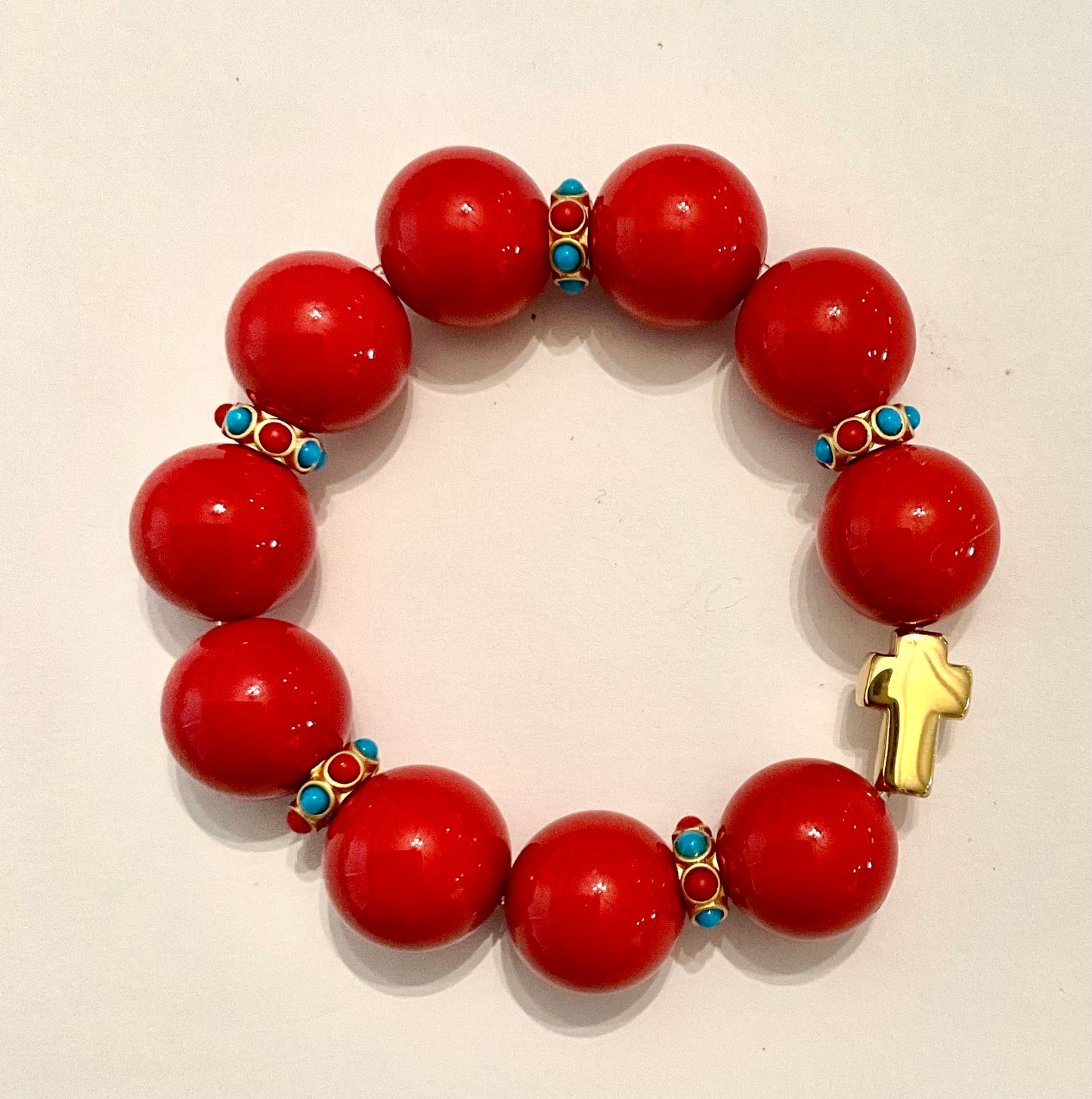 Red beaded bracelet with gold and turquoise accents on a beige background