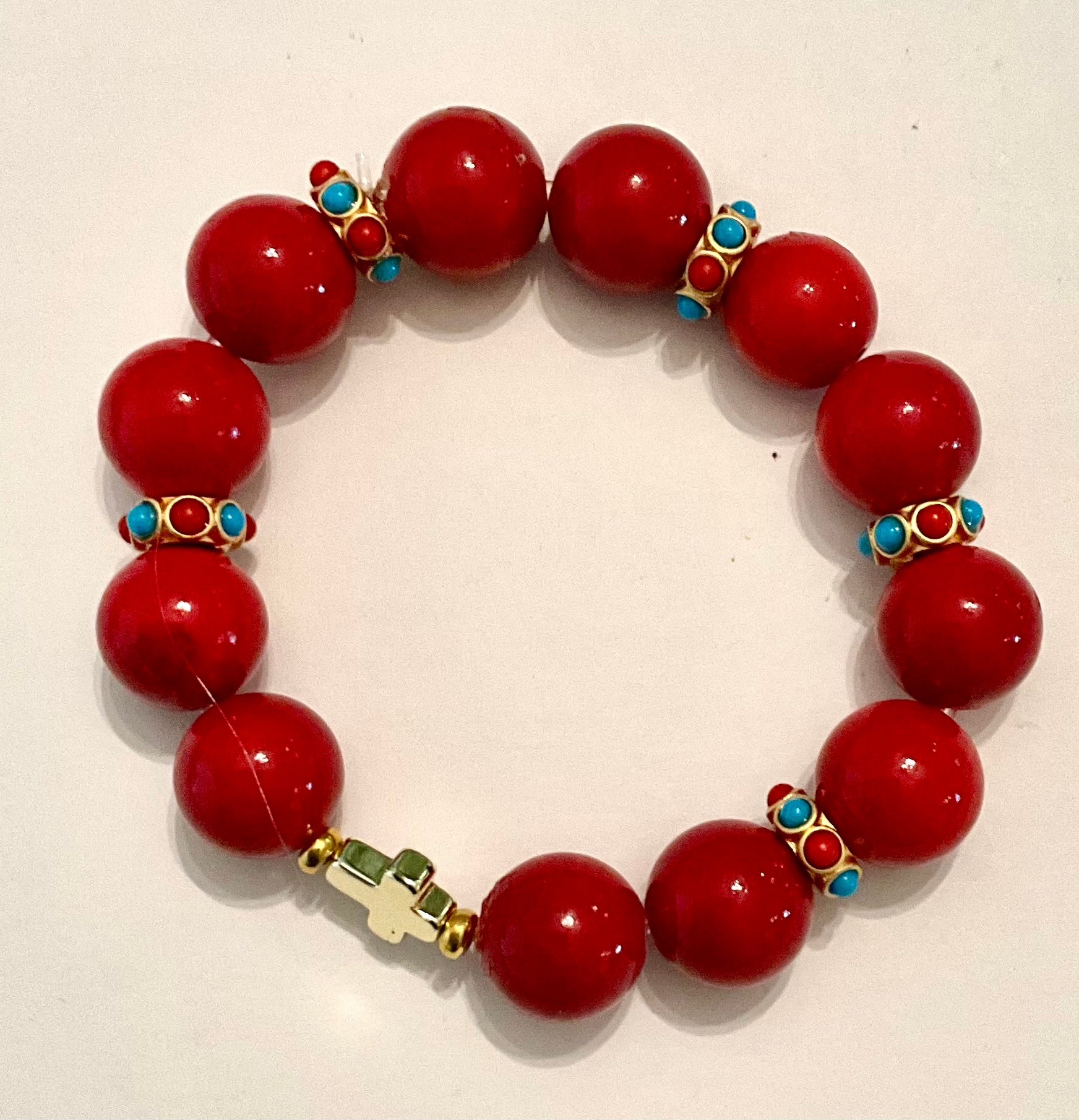 Red beaded bracelet with gold and turquoise accents on a white background