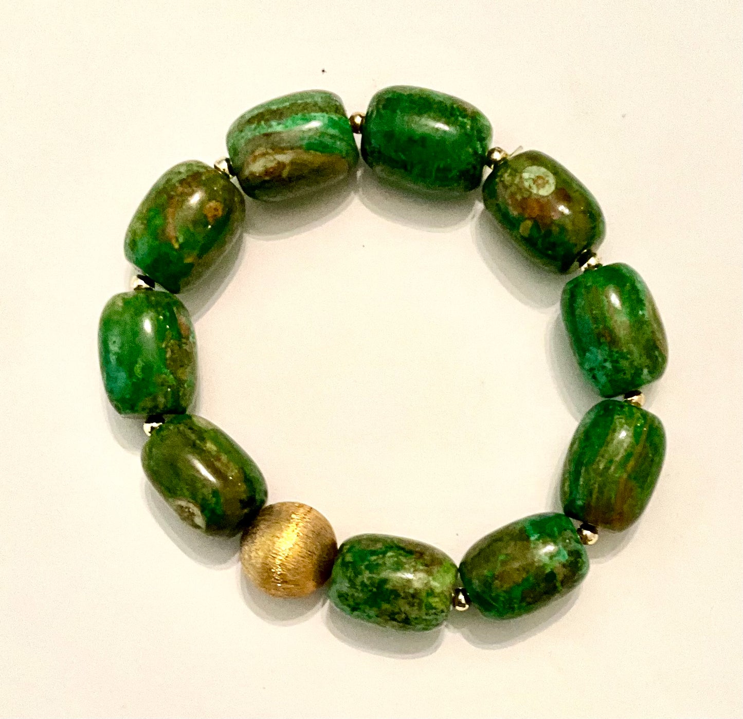 Green beaded bracelet with a gold accent on a white background