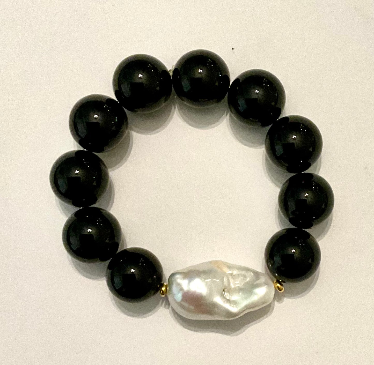 Black beaded bracelet with a central white pearl on a light background