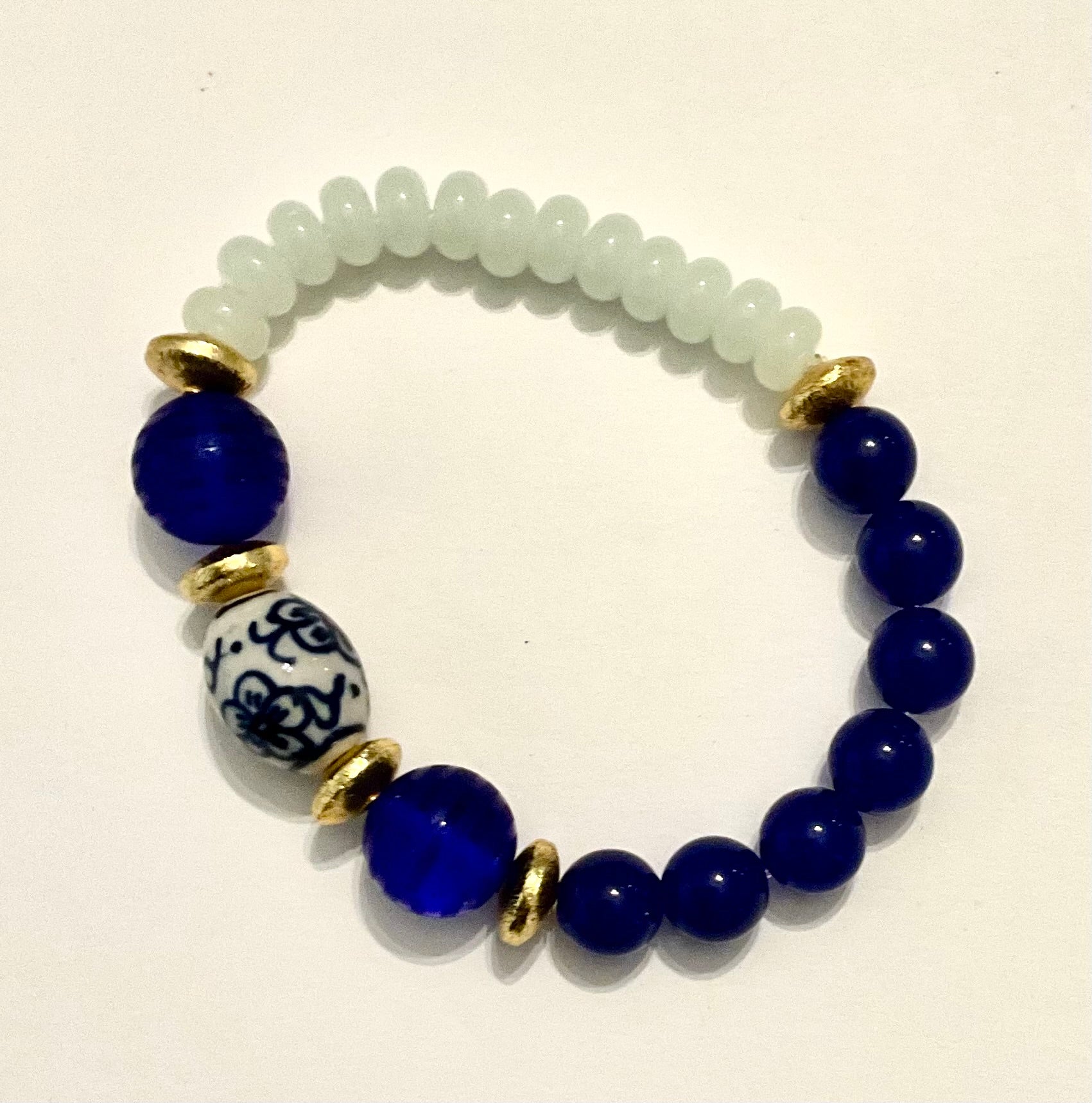 Bracelet with blue beads and a decorative gold and white bead on a light background