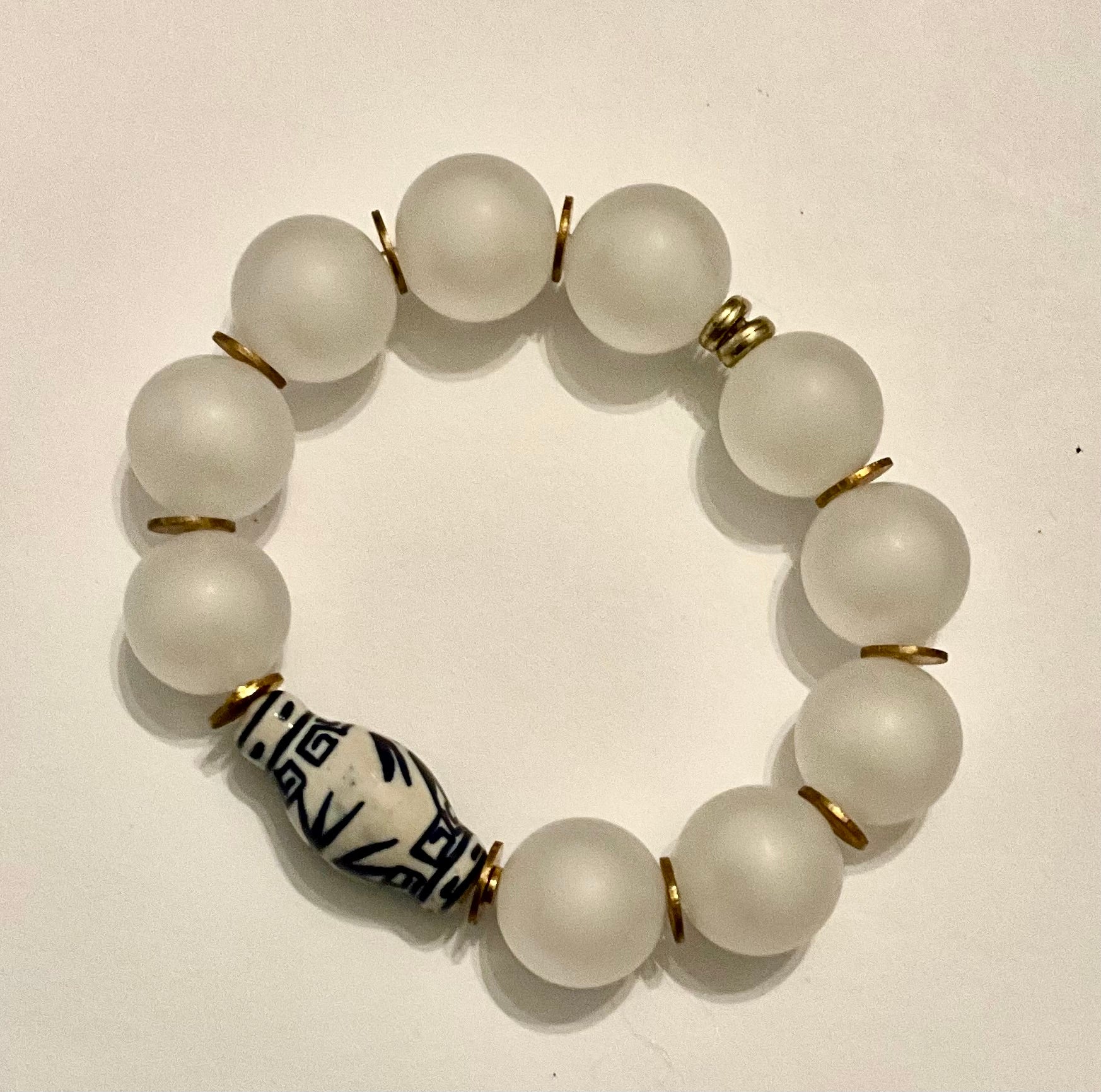 White beaded bracelet with a patterned central bead on a beige background