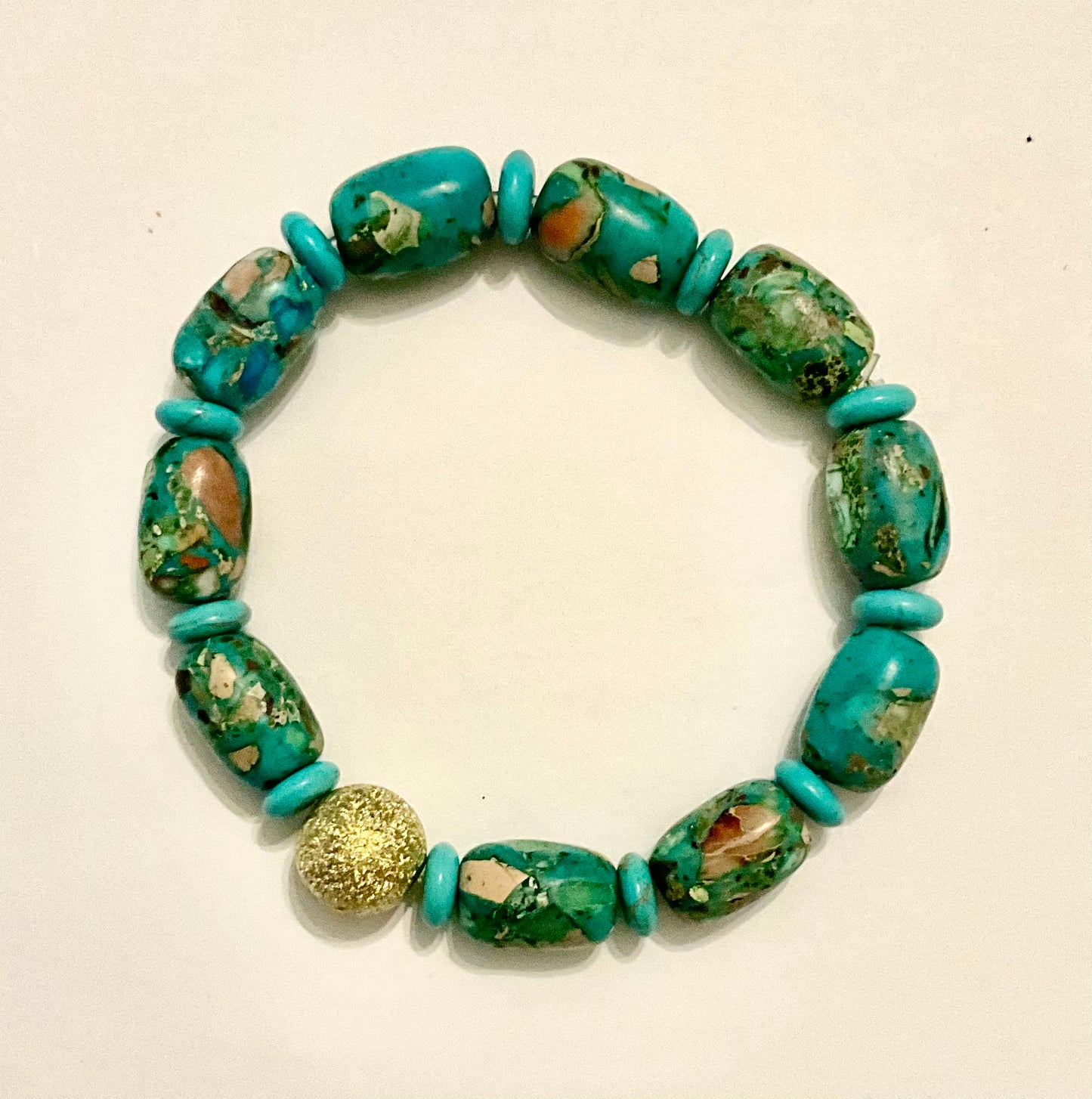 Turquoise beaded bracelet with a gold accent on a beige background