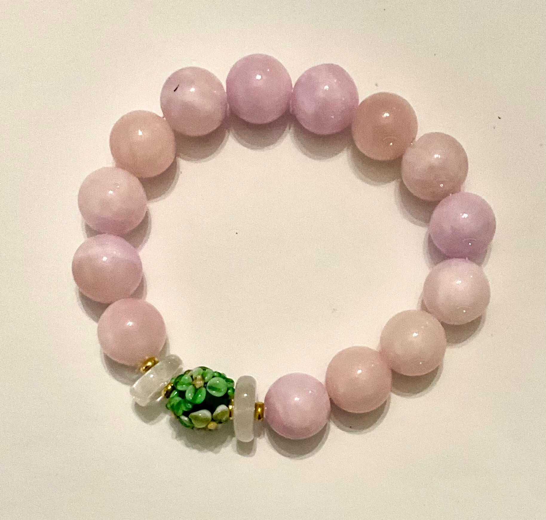 Beaded bracelet with pink beads and a green and white bead on a light background