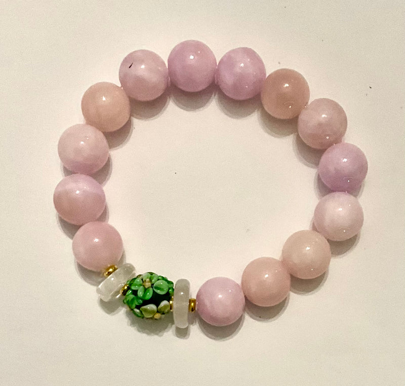 Beaded bracelet with pink beads and a green and white bead on a light background