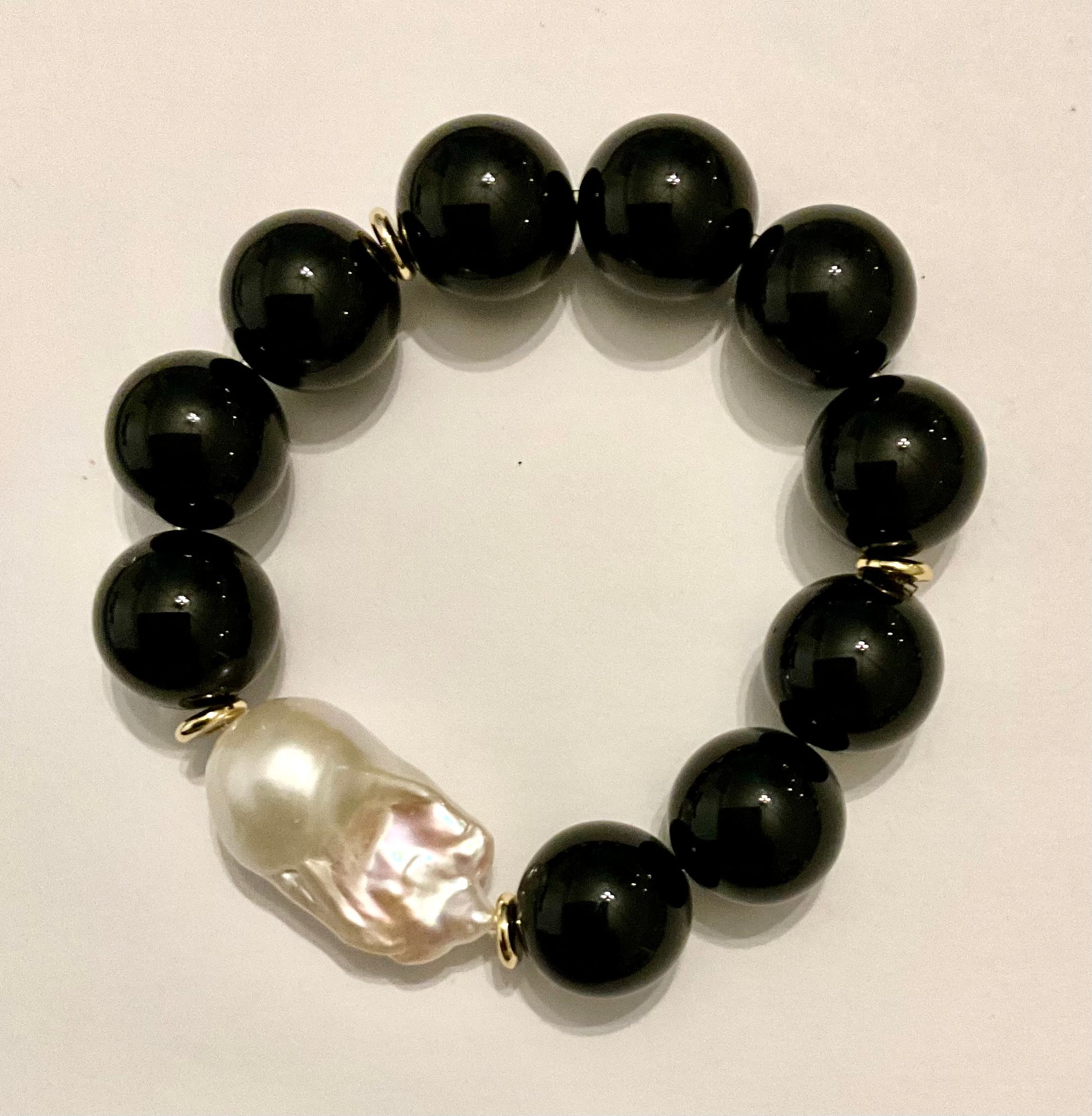 Black beaded bracelet with a central pearl on a light background