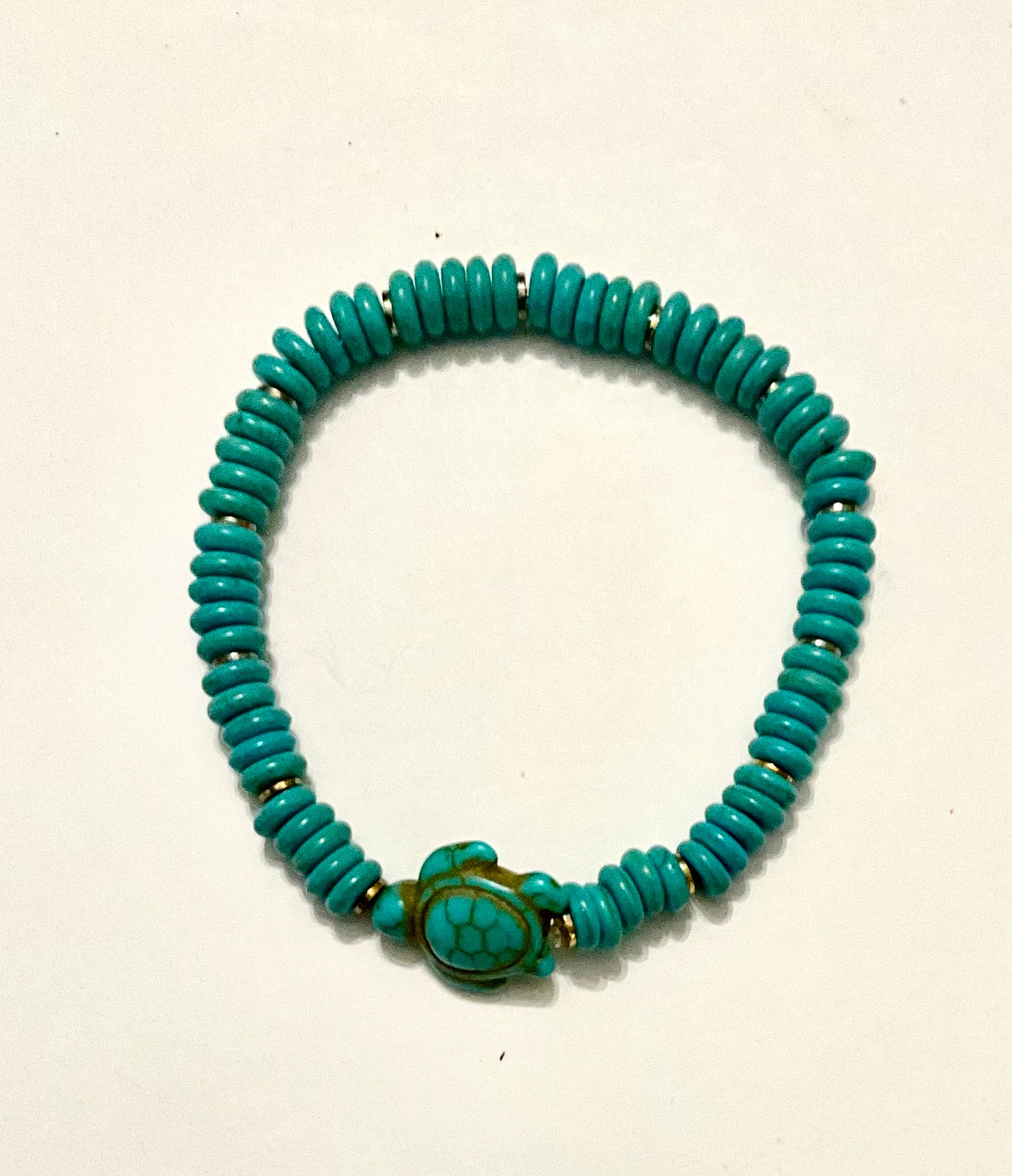 Turquoise beaded bracelet with a turtle charm on a light beige background