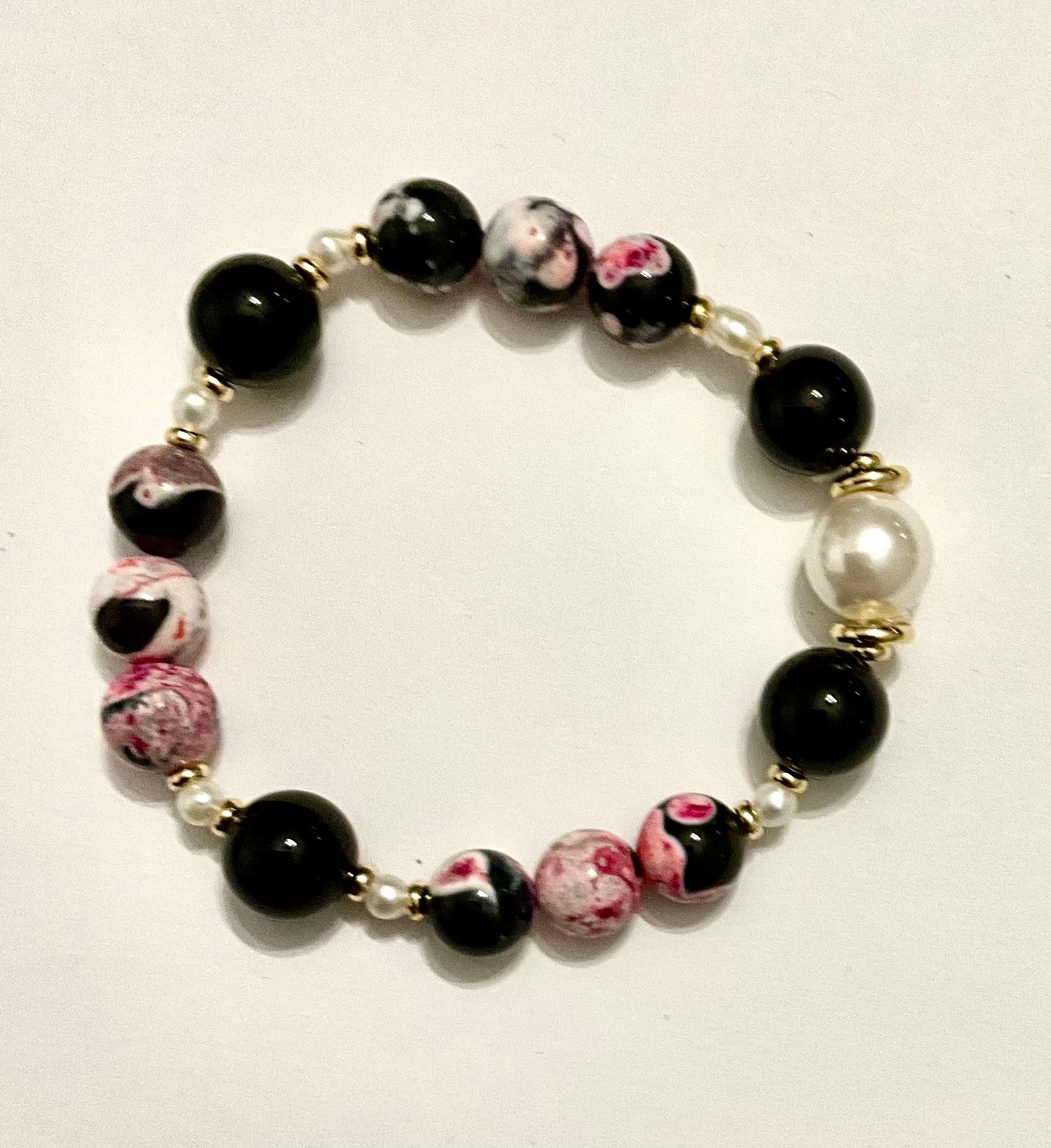 Beaded bracelet with black, pink, and white beads on a light background