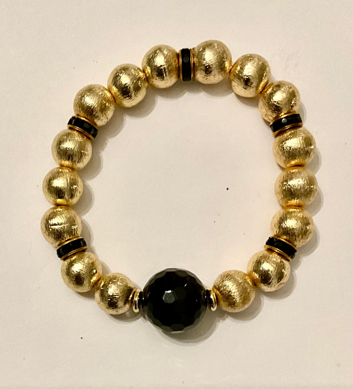 Gold beaded bracelet with a central black bead on a white background