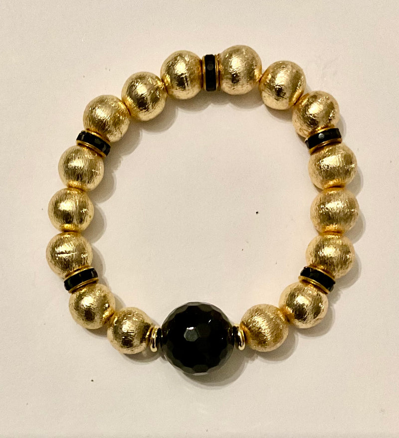 Gold beaded bracelet with a central black bead on a white background