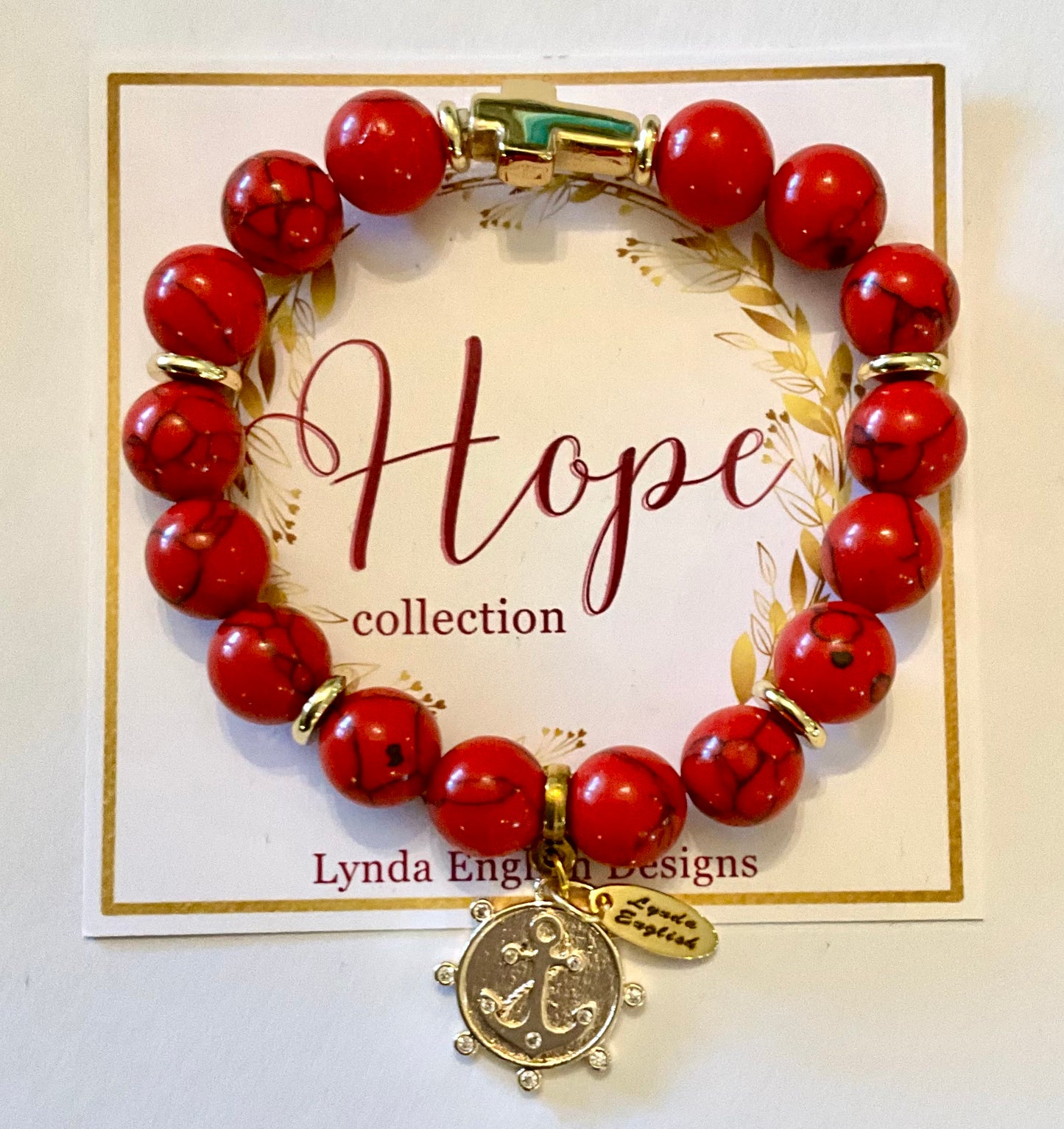 Red beaded bracelet with a gold charm on a 'Hope collection' card by Lynda English Designs.