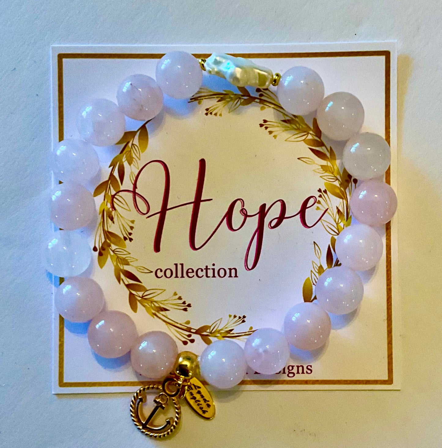 White beaded bracelet with a gold charm on a 'Hope collection' card.